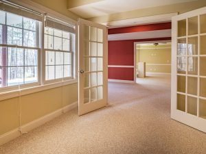 Bright and spacious empty room featuring French doors, large windows, and a warm color palette.
